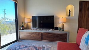 Una sala de estar con una gran televisión de pantalla plana, dos lámparas de pared, un sofá rojo y una alfombra estampada.