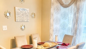 Een eetzaal met een tafel voor vier personen, voorzien van een beige tafelkleed, rode borden en een kaarsdecoratie.