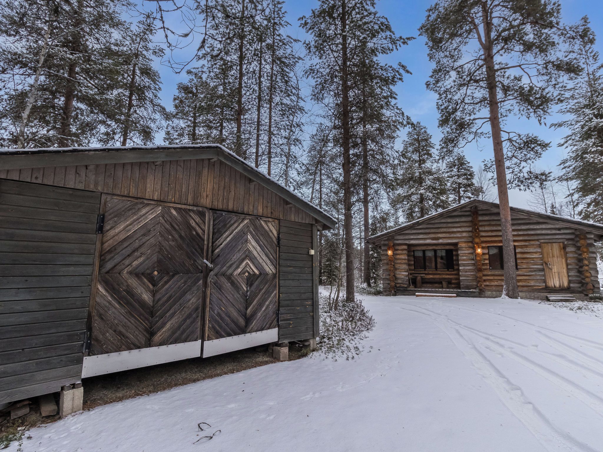 Una cabaña con un gran puerta de madera y una puerta más pequeña, rodeada de nieve y altos árboles.