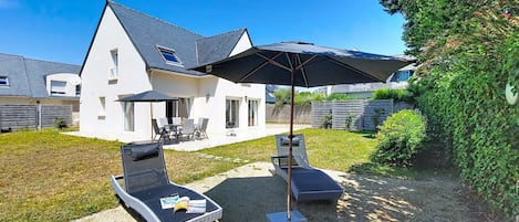 Una casa con un patio que tiene dos sillones, una mesa y una sombrilla grande.