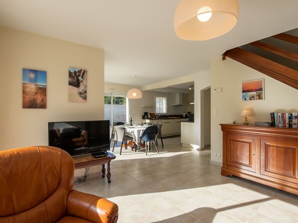 A modern living room with a leather sofa, a TV, and a dining area with a table and chairs.