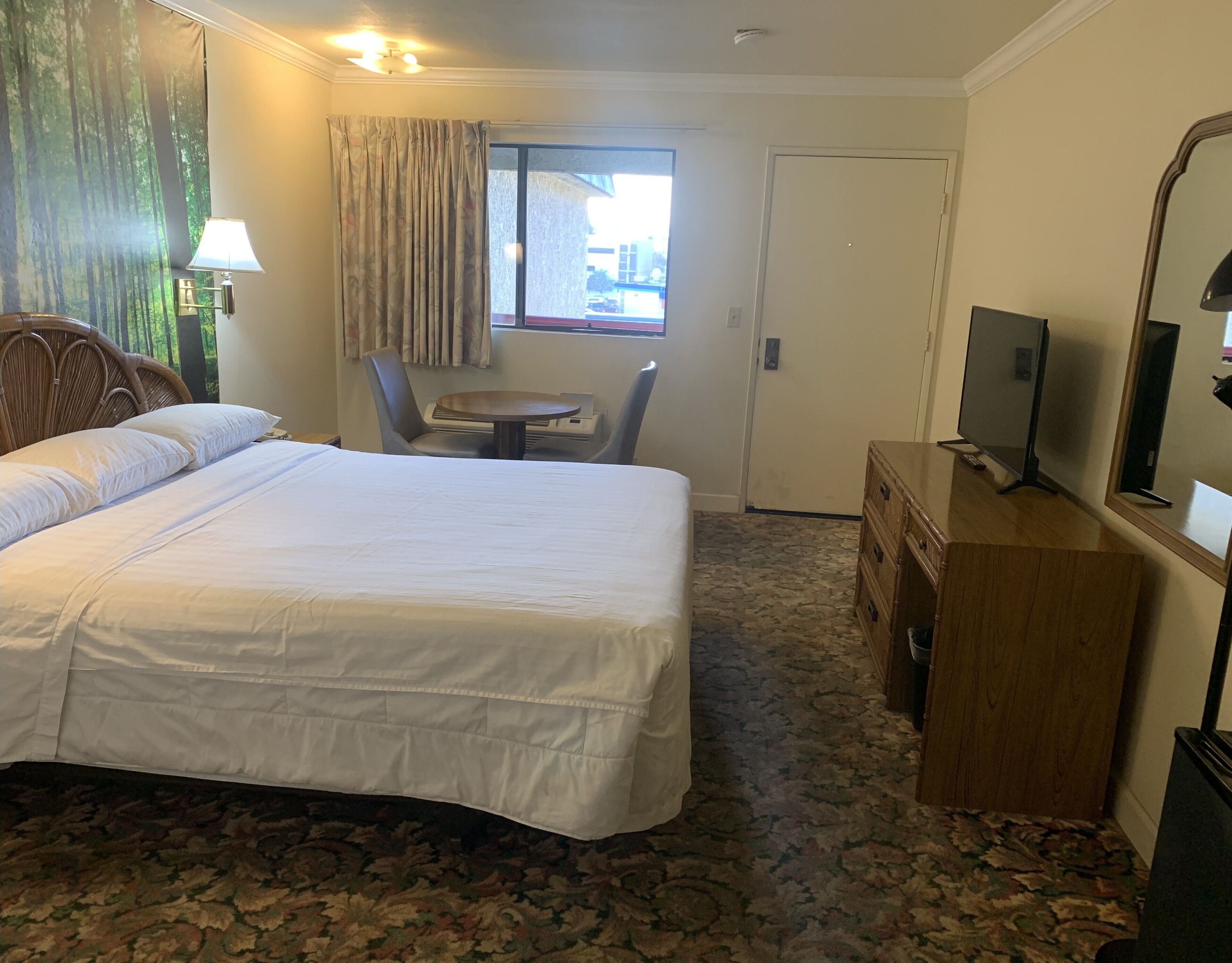 A hotel room with a large bed, a desk, a chair, a television, and a window with curtains.