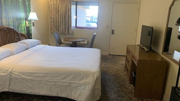A hotel room with a large bed, a desk, a chair, a television, and a window with curtains.