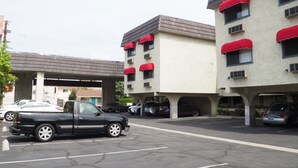 Un estacionamiento con varios coches, un edificio con toldos rojos y un paseo techado.