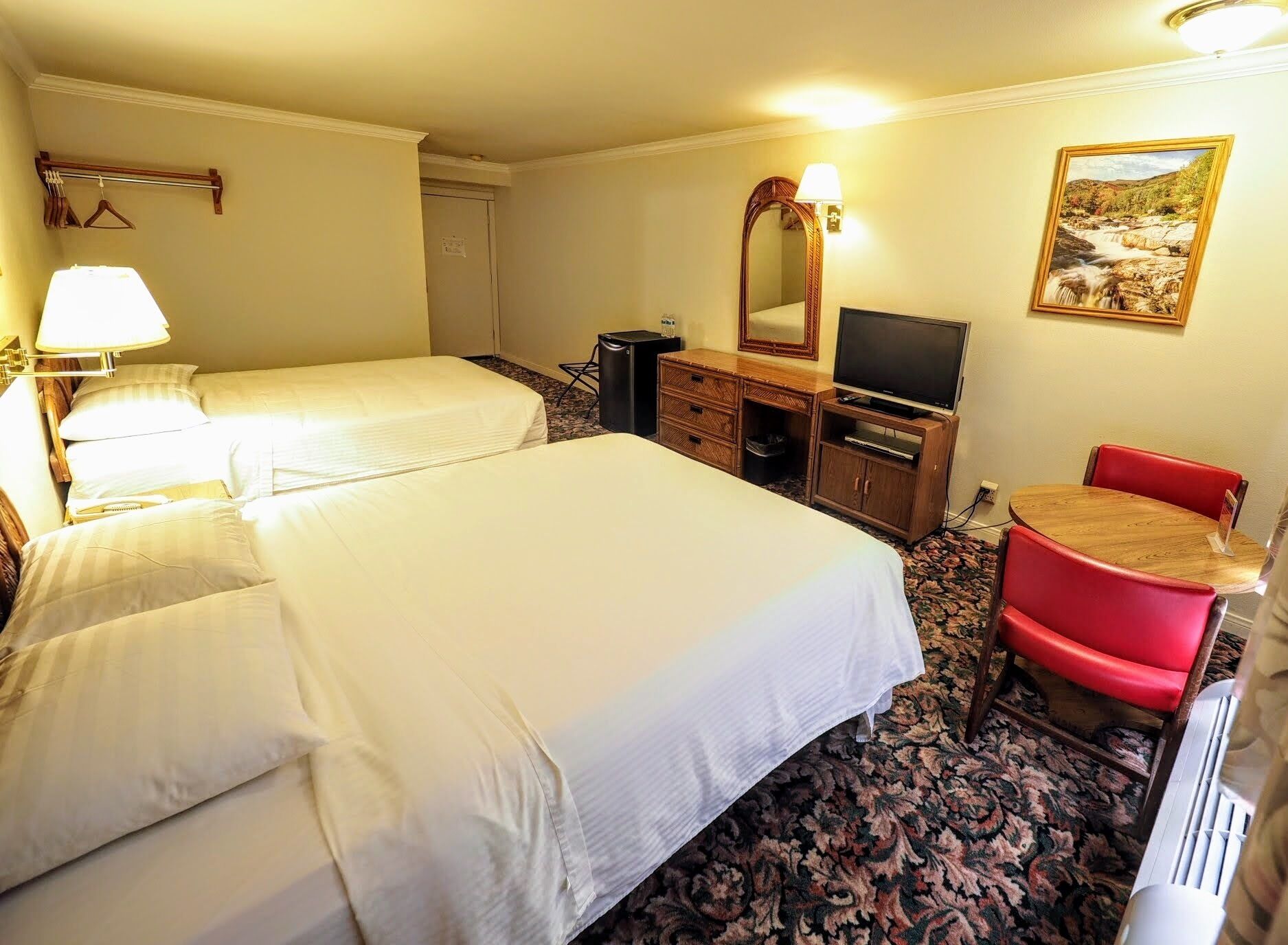 A hotel room with two beds, a desk with a TV, a chair, a dresser, and a painting on the wall.