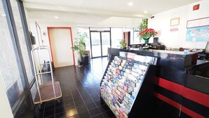 Un área de recepción con piso de baldosas, un mostrador de recepción con un atril para revistas, y una puerta que da a otra habitación.