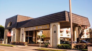 Un hotel con un llamativo letrero que dice 'Grand Inn', una señal de límite de velocidad de 35 millas por hora, y un estilo arquitectónico clásico con techo plano y ventanas arqueadas.