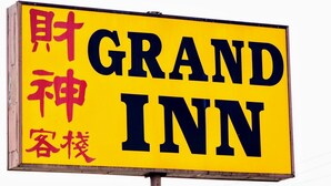 A yellow sign with the words "GRAND INN" in large black letters, and smaller red Chinese characters above and below.