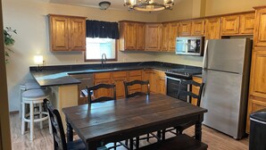 A kitchen with wooden cabinets, a stainless steel refrigerator, a microwave, a dining table with chairs, and a chandelier. - Spacious 5-bedroom house with WiFi, AC in charming Arvada (Arvada)