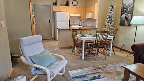 Una sala de estar con un sillón grande, una mesa de comedor con sillas, una zona de cocina y un pequeño árbol de Navidad.