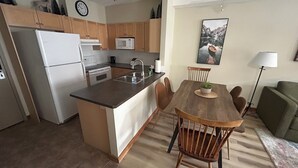 Una cocina equipada con refrigerador, microondas y estufa. Se observa una mesa de comedor con sillas y una lámpara.