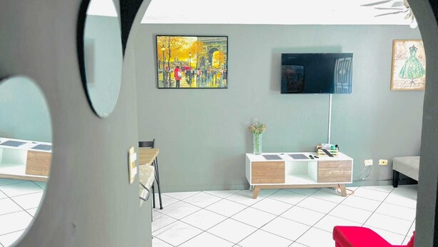A room with a tiled floor, a TV mounted on the wall, a painting, and a red chair.