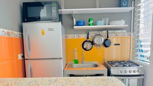 A kitchen with a refrigerator, microwave, stove, sink, and hanging pots.