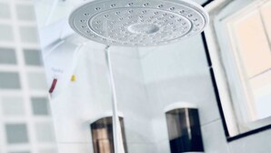 A shower with a rain-like water feature, a hand dryer, and a soap dispenser on the wall.