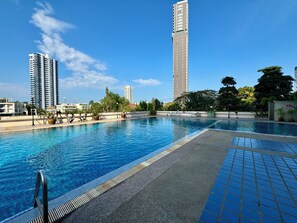 Una piscina con agua azul cristalina, rodeada de plantas en macetas y un deck de baldosas.