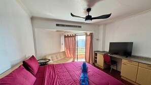 Habitación de hotel con cama, escritorio, televisor y balcón con cortinas.
