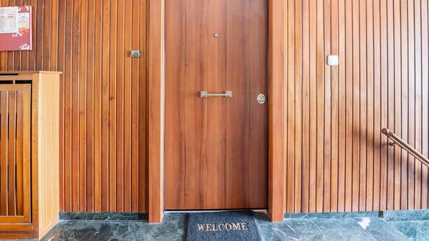 A wooden door with a handle and a keyhole, flanked by vertical wooden panels and a welcome mat at the entrance. - Athenian Entertainment & Relaxation Hub (Athens)