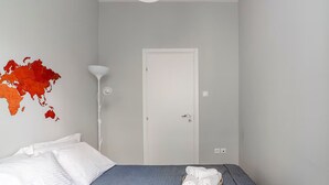 A bedroom with a bed, white pillows, a folded towel, a world map on the wall, and a door. - Athenian Entertainment & Relaxation Hub (Athens)
