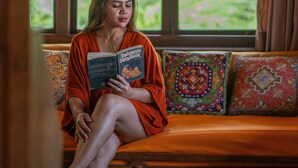A person sitting on a wooden bench with colorful cushions, reading a book titled "Indonesia Handbook."