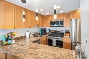 Una cucina moderna con mobili in legno, piani in granito, elettrodomestici in acciaio inossidabile e luci a sospensione.