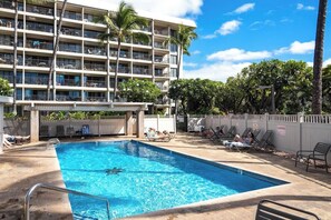 Un espace piscine d’hôtel avec une piscine à l’eau cristalline, des chaises longues et un immeuble à plusieurs étages doté de balcons.