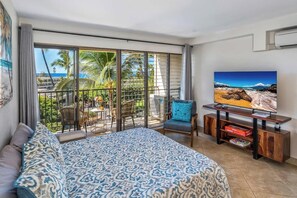 Ein Hotelzimmer mit einem großen Bett, einem Fernseher, einem Balkon mit Meerblick und einem Essbereich mit Stühlen und einem Tisch.