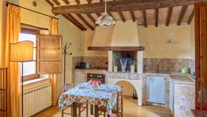 A rustic kitchen with wooden beams, a dining table with chairs, a radiator, and a small sink. - Borgo  Fastelli - FASTELLI NOCE (Sarteano)