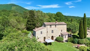 A stone building with a tiled roof, surrounded by lush greenery and hills. - Borgo  Fastelli - FASTELLI NOCE (Sarteano)