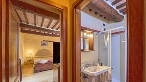 A bedroom with a bed, bedside table, and a nightstand. The bathroom includes a sink, mirror, and shower. - Borgo  Fastelli - FASTELLI NOCE (Sarteano)