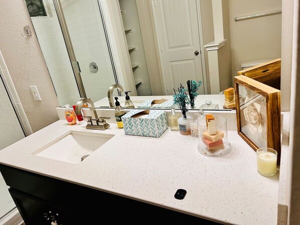 Un baño con lavabo blanco, espejo, dispensador de toallas y una foto enmarcada sobre el mostrador.