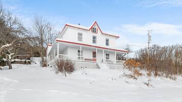 Stunning two-story home with a charming front porch and red door, set amidst a serene winter landscape.