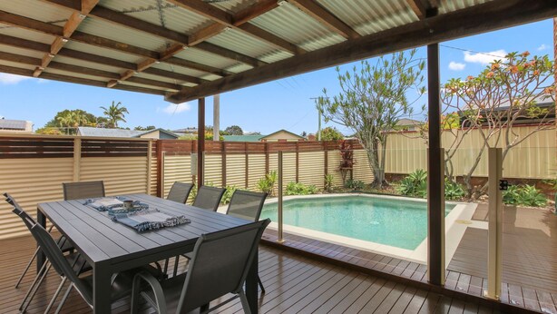 A covered outdoor area with a pool, wooden deck, and a table with chairs. - Bren Place, 6, Battery Hill (Battery Hill)
