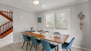 A dining area with a wooden table, four blue chairs, a ceiling fan, and a window with blinds. - Bren Place, 6, Battery Hill (Battery Hill)