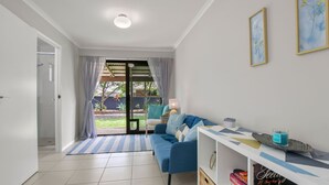 A living room with a blue sofa, a coffee table, and a bookshelf. There is a sliding glass door leading to a garden. - Bren Place, 6, Battery Hill (Battery Hill)