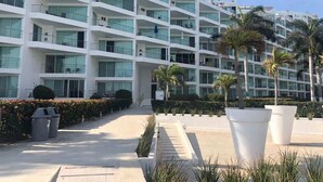A multi-story hotel with balconies, large windows, and a landscaped courtyard with palm trees. - Area Ocean, Affordable 1BR Studio, Beachfront Resort, Pools, Snack Bar, & Balcony (Nuevo Vallarta)