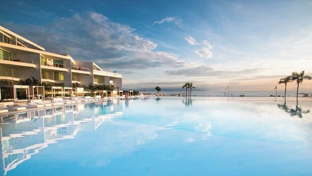 A modern hotel with a large infinity pool, multiple balconies, and a view of the ocean. - Area Ocean, Affordable 1BR Studio, Beachfront Resort, Pools, Snack Bar, & Balcony (Nuevo Vallarta)