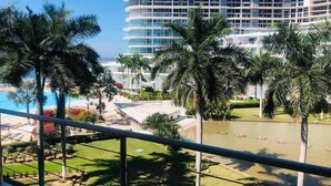 A hotel with a pool area, palm trees, and a large building in the background. - Area Ocean, Affordable 1BR Studio, Beachfront Resort, Pools, Snack Bar, & Balcony (Nuevo Vallarta)