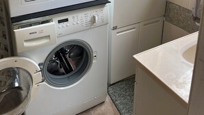 Uma lavanderia compacta com máquina de lavar e secadora Bosch Classic, uma pia pequena e uma janela com vista para o verde.