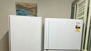 Duas geladeiras brancas com etiqueta de classificação energética Samsung, localizadas em um quarto com piso de madeira e um quadro na parede.