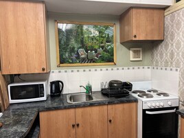 Una cocina con armarios de madera, microondas, hervidor, lavaplatos y estufa.