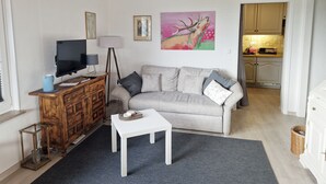Ein Wohnzimmer mit einer Couch, einem Couchtisch, einem Fernseher und einem Bild an der Wand.