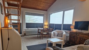Ein gemütliches Wohnzimmer mit Holzbalkendecke, einem Essbereich mit Tisch und Stühlen, einer Couch, einem Fernseher und einem Kamin.