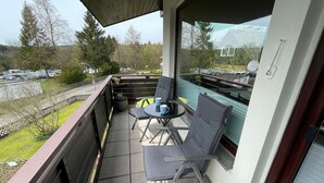 Ein Balkon mit zwei Stühlen und einem Tisch, Blick auf einen Parkplatz und ein Gebäude mit Satellitenschüssel.