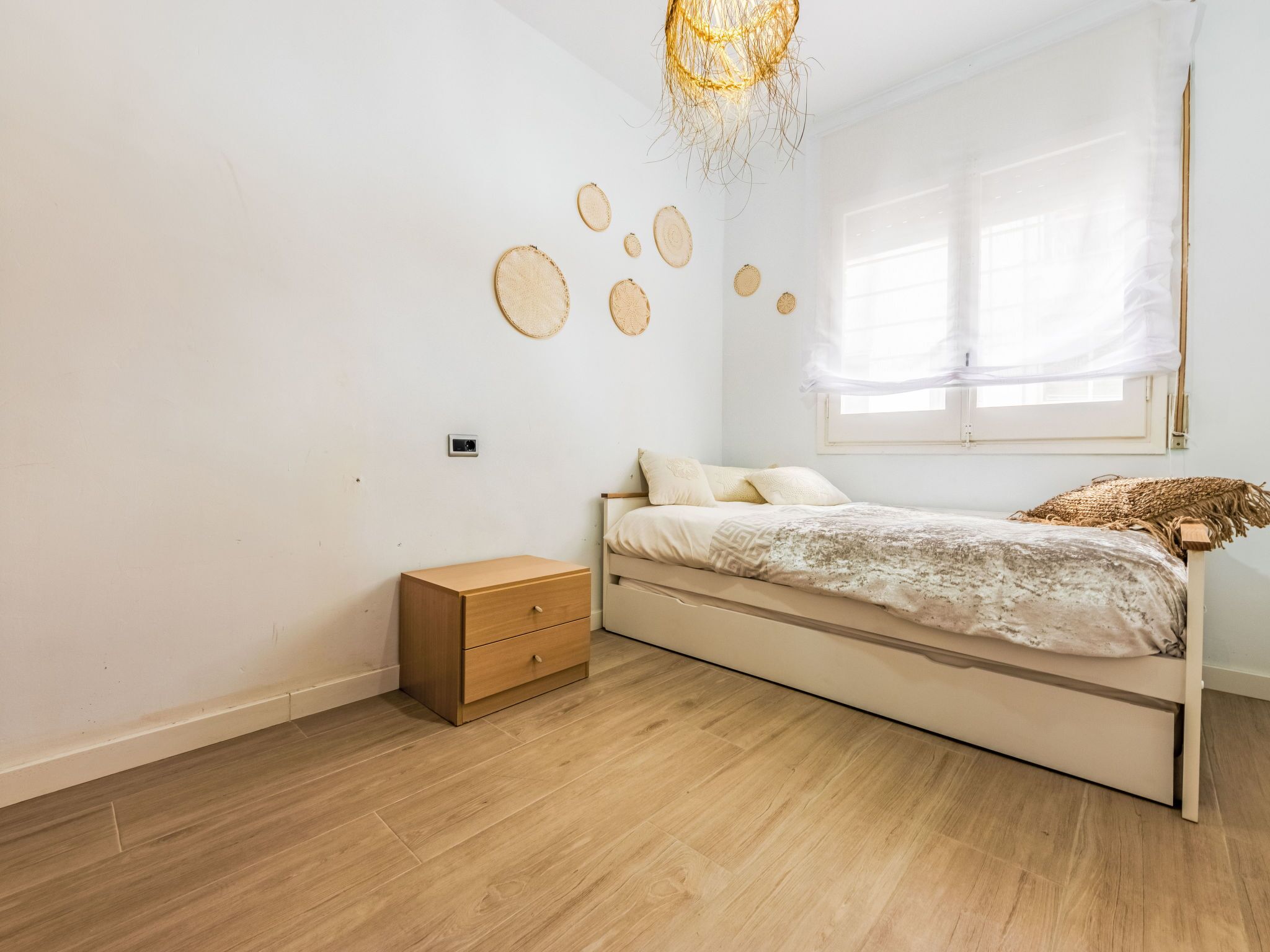 A minimalist bedroom with a wooden bed, a small wooden nightstand, and a unique wall decoration.