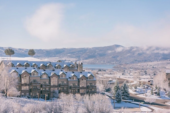 Ein mehrgeschossiges Hotel mit symmetrischer Fassade, Balkonen und Blick auf einen See und Berge.