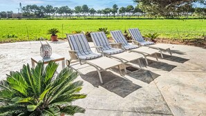 Un patio con cuatro sillones reclinables a rayas, una mesa y un farol decorativo.
