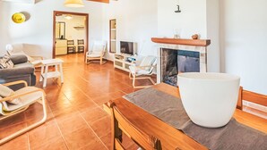 Amplia sala de estar con chimenea, vigas de madera en el techo y un recipiente blanco grande sobre una mesa.