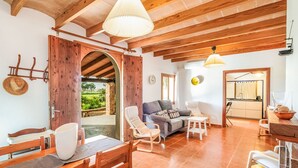 Un salón amplio con techo de madera, un sofá, una mesa de comedor con sillas y una cocina al fondo.