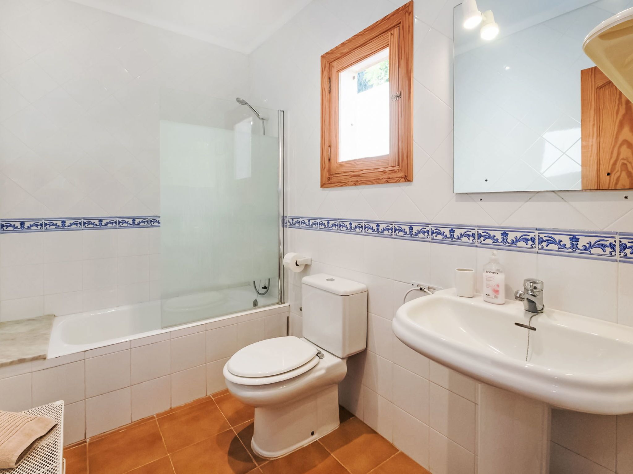 A bathroom with a glass-enclosed shower, a toilet, a sink, and a mirror.