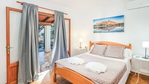 A bedroom with a wooden bed, grey curtains, a painting of a landscape, and a nightstand with a lamp. - Villa Sa Rapita by Interhome (Sa Rápita)